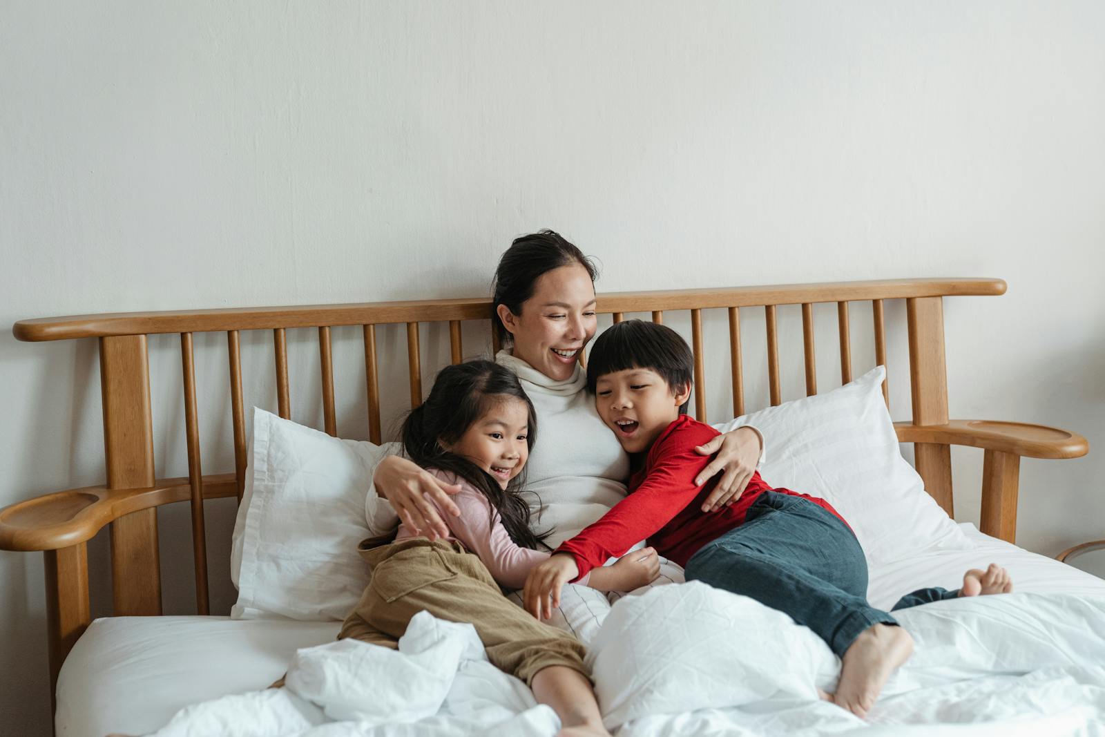 Cheerful ethnic mother hugging children lying in bed